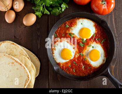 Shakshuka mit Eiern, Tomaten und Petersilie in einer gusseisernen Pfanne. Stockfoto