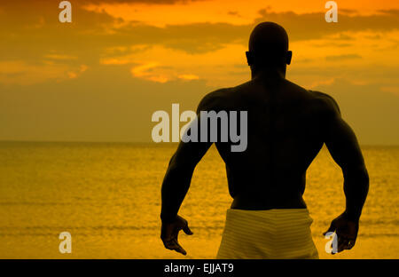 Silhouette eines Bodybuilders posiert auf den Sonnenaufgang am Strand, Ausbildung in den Morgen, starken Mann zeigt seine Muskeln Stockfoto