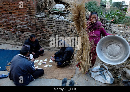 Nepali Frau arbeitet als Männer spielen Karten in der Newar Dorf Bungamati, die in Kathmandu, Nepal liegt. Stockfoto