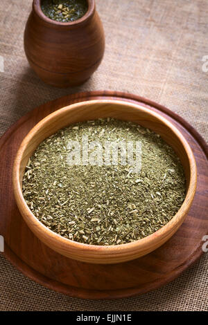 Südamerikanischen Yerba Mate (Mate-Tee) getrocknete Blätter in Holzschale mit einer hölzernen Mate Tasse mit Tee gefüllt Stockfoto