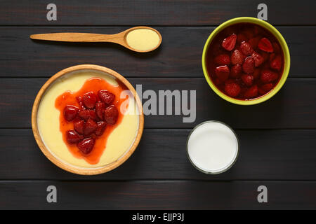 Overhead Schuss von Grieß-Pudding mit Erdbeeren Kompott serviert in Holzschale, fotografiert auf dunklem Holz mit natürlichem Licht Stockfoto