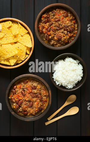 Overhead Schuss von zwei Schalen mit Chili Con Carne mit Reis und Tortilla-Chips, fotografiert auf dunklem Holz mit natürlichem Licht Stockfoto