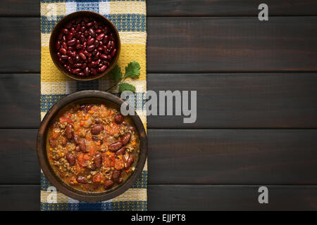 Overhead Schuss von Chili Con Carne und getrocknete Kidneybohnen in Schalen auf Küchentuch, fotografiert auf dunklem Holz mit natürlichem Licht Stockfoto