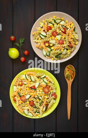 Overhead Schuss aus zwei Platten von vegetarischer Nudelsalat gemacht Tricolor Fusilli, Zuckermais, Gurken und Cherry Tomaten Stockfoto