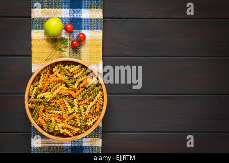 Obenliegende Aufnahme von rohen Tricolor Fusilli oder Rotini Nudeln (traditionelle, Tomaten und Spinat Geschmack) in Holzschale mit Zutaten Stockfoto