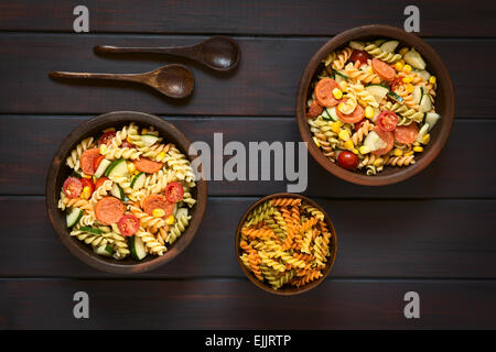 Overhead Schuss von zwei rustikale Schalen mit Nudelsalat gemacht der Trikolore Fusilli, Mais, Gurke, Cherry-Tomaten und Wurst Stockfoto