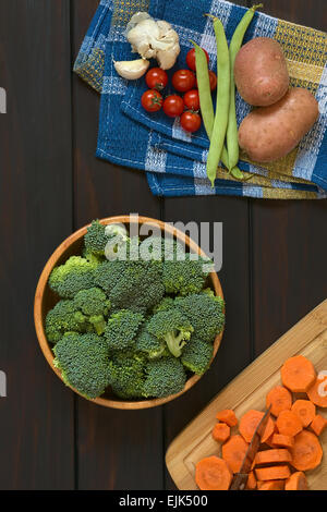 Overhead Schuss von frischem rohen Broccoli-Röschen in Holzschale mit anderem Gemüse rund um Stockfoto
