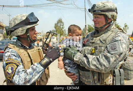 Capt Clay White rechts, Kommandant der Firma C, 2. Bataillon, 505. Fallschirm-Infanterie-Regiment, 3rd Brigade Combat Team, 82nd Airborne Division, Multi-National Division-Bagdad, spricht zu einem nationalen Polizisten, als er ein irakischen Kind trägt eine Anschluss an eine Schule Versorgung Verbreitung am 1.April im Bezirk 9 Nissan von östlichen Bagdad NP-Uniform trägt. Weiß und Fallschirmjäger wurden von irakischen Beamten eingeladen zur Teilnahme an Orphan Nationalfeiertag in Irak. Irakische Beamten ausgehändigt Kleidung und Schulmaterialien zu mehr als 60 Kinder in einer 9 Nissan-Schule. Stockfoto