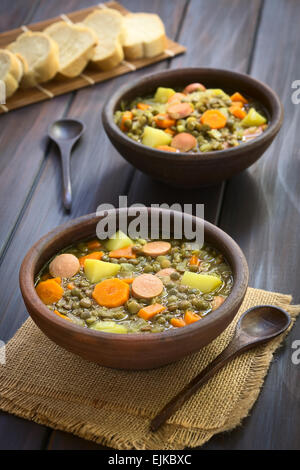 Zwei rustikale Schalen mit Linsensuppe gemacht mit Kartoffel, Karotte, Zwiebel und Wurst Scheiben mit Scheiben Baguette-Brot in den Rücken Stockfoto