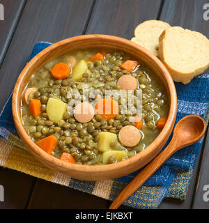 Holzschale Linsensuppe mit Kartoffeln, Karotten, Zwiebeln und Wurst Scheiben, fotografiert auf dunklem Holz mit natürlichem Licht gemacht Stockfoto