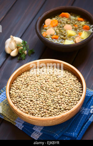 Rohe Linsen (lat. Lens Culinaris) in Holzschale mit einer rustikalen Schüssel Linsensuppe (mit Linsen, Karotten, Kartoffeln, Wurst gemacht) Stockfoto