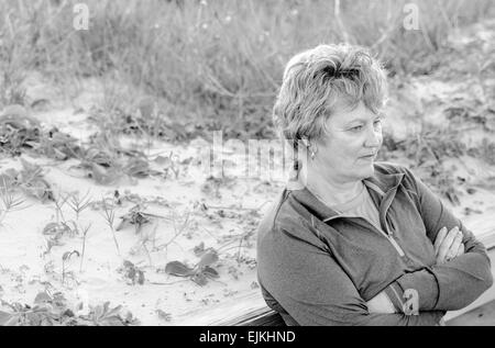 Ältere Frau entspannt warten beim schiefen gegen ein Geländer in Strandnähe in schwarz / weiß Stockfoto