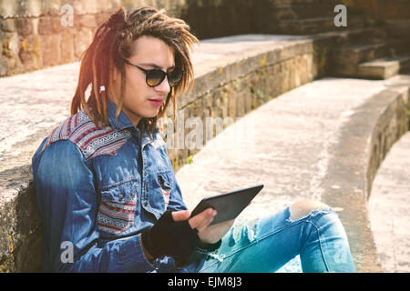 Freelancer-Kerl mit Dreadlocks auf Treppe sitzend mit digital-Tablette eingeben warm Nachrichtenfilter angewendet Stockfoto