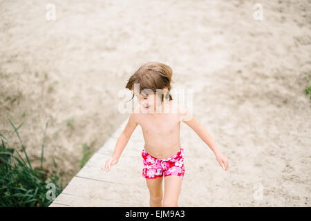Kleines Mädchen am Strand an heißen Sommertag. Spaß im Urlaub. Mädchen zu Fuß auf der Holzterrasse am See