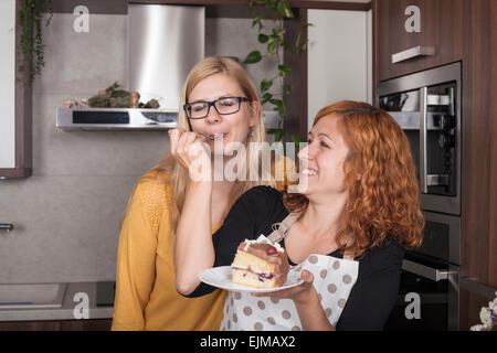 Freuen uns Freundinnen Kuchen und füttern einander in der Küche zu Hause. Stockfoto