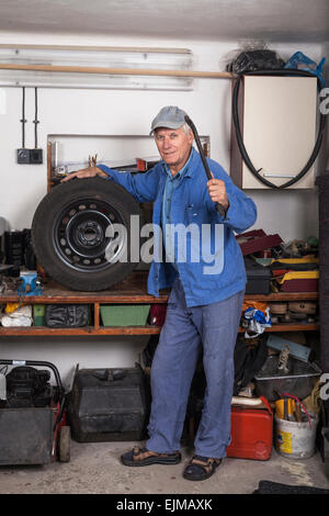 Porträt von senior Arbeiter mit einem Reifen und Werkzeug in der Garage stehen. Stockfoto