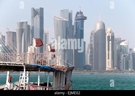 Katar Fahnen flattern auf einem Dhau-Boot in den Persischen Golf mit der Skyline von Doha im Hintergrund. Stockfoto