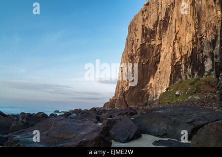 Rote Sonne auf Felswand und grauen Steinen am Strand bei Sonnenaufgang Stockfoto