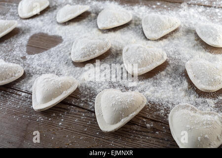 Roh-Ravioli in Form von Herzen, bestreuen mit Mehl, auf dunklen hölzernen Hintergrund. Knödel kochen. Geringe Schärfentiefe. Stockfoto