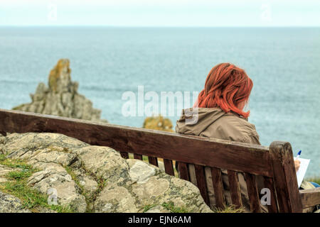 Rothaarige junge Frau sitzend auf einer Bank auf dem SW Küstenweg in Polperro, Südost Cornwall, Südwestengland, UK. Stockfoto