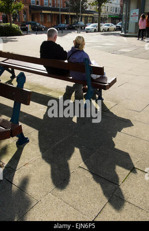 Niedrige Sonne wirft Schatten von Mann und Frau sitzen auf Bank in Llandudno, Wales, UK Stockfoto