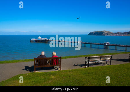 Mann und Frau sitzen in Happy Valley Gardens Blick auf Llandudno Pier und Little Orme, Conwy, Nordwales. Stockfoto