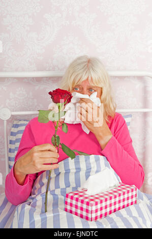 Traurige Frau in rosa Pyjama im Bett sitzend, mit einer Rose und Gewebe Stockfoto