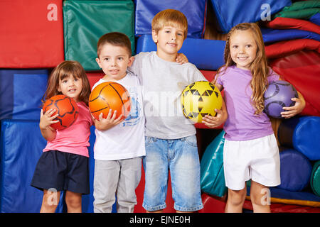 Glückliche Gruppe von Kindern mit verschiedenen Bällen in der Turnhalle des Kindergartens Stockfoto