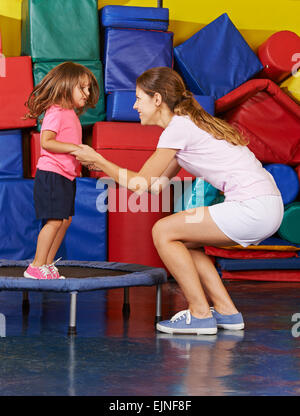 Mädchen springen auf dem Trampolin mit Kindergärtnerin beim Kinder-Sport Stockfoto