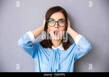 Überrascht Geschäftsfrau auf grauem Hintergrund. Im blauen Hemd und Brille tragen. Ihre Ohren mit den Händen bedeckt. Offenem Mund. Loo Stockfoto