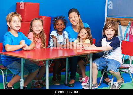 Glückliche Kinder sitzen zusammen mit Kindergärtnerin am Tisch im kindergarten Stockfoto