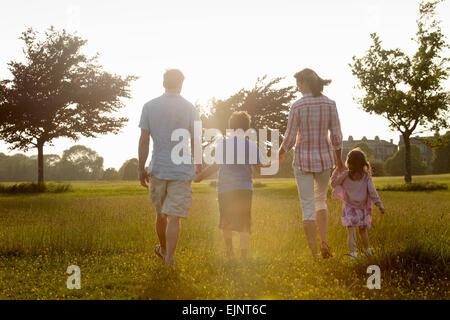 Eine Familie, zwei Eltern und zwei Kinder hand in hand gehen über den Rasen im Freien im Sommer.