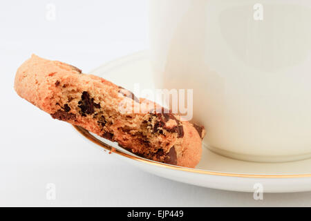 Chocolate Chip Keks mit einem Biss auf der Untertasse mit einer Tasse englischen Tee herausgenommen. England, UK, Großbritannien Stockfoto