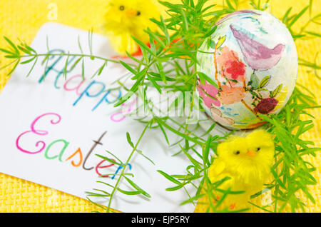 Handgemalte Decoupage Easter Egg auf Holzoberfläche mit einer Frohe Ostern-Karte und zwei Kaninchen Spielzeug Stockfoto