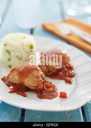 Hähnchenschenkel in einer Tomaten-Zwiebel Sauce serviert mit einem Turm von Reis auf einem rustikalen blau gewaschenen Lattenrost Holztisch Stockfoto