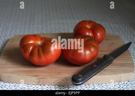 RAF Tomaten (Solanum Lycopersicum) und Messer auf hölzernen Schneidebrett auf Tischdecke Stockfoto