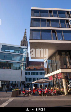 Menschen in einer Caféterrasse in Hans Und Sophie Schol Platz mit dem Münster in der Abenddämmerung Stockfoto
