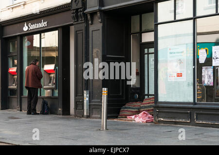 Man Bargeld von einer Bank Geldautomat neben einem Obdachlosen-Bett in einem stillgelegten Shop Eingang Stockfoto