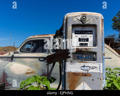 Eine 1947 Chrysler Limousine 4 Türen rosten mit verblassten Farben sitzt vor zwei alten Stil-Zapfsäulen an der Tankstelle geparkt. Stockfoto