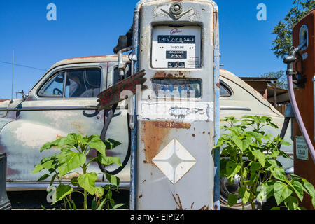 Eine 1947 Chrysler Limousine 4 Türen rosten mit verblassten Farben sitzt vor zwei alten Stil-Zapfsäulen an der Tankstelle geparkt. Stockfoto