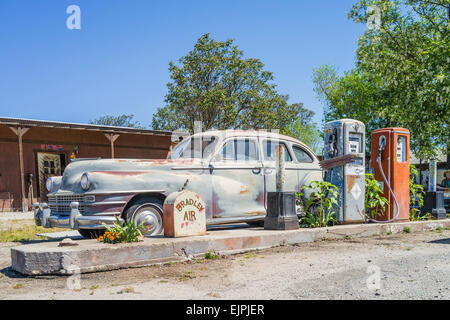 Eine 1947 Chrysler Limousine 4 Türen rosten mit verblassten Farben sitzt vor zwei alten Stil-Zapfsäulen an der Tankstelle geparkt. Stockfoto