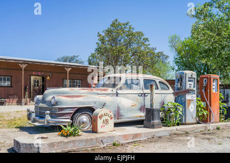 Eine 1947 Chrysler Limousine 4 Türen rosten mit verblassten Farben sitzt vor zwei alten Stil-Zapfsäulen an der Tankstelle geparkt. Stockfoto