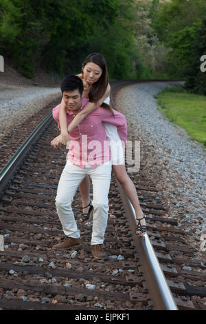 Romantisches asiatische paar spielen im Freien auf Eisenbahnschienen, reitet sie auf dem Rücken in einem "Huckepack" Mode Stockfoto