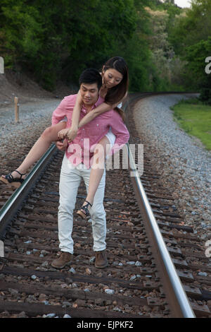 Romantisches asiatische paar spielen im Freien auf Eisenbahnschienen, reitet sie auf dem Rücken in einem "Huckepack" Mode Stockfoto