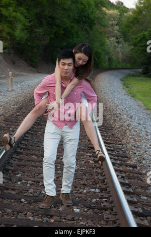 Romantisches asiatische paar spielen im Freien auf Eisenbahnschienen, reitet sie auf dem Rücken in einem "Huckepack" Mode Stockfoto
