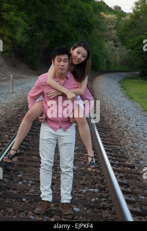 Romantisches asiatische paar spielen im Freien auf Eisenbahnschienen, reitet sie auf dem Rücken in einem "Huckepack" Mode Stockfoto
