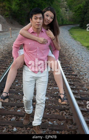 Romantisches asiatische paar spielen im Freien auf Eisenbahnschienen, reitet sie auf dem Rücken in einem "Huckepack" Mode Stockfoto