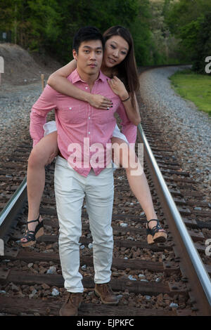 Romantisches asiatische paar spielen im Freien auf Eisenbahnschienen, reitet sie auf dem Rücken in einem "Huckepack" Mode Stockfoto