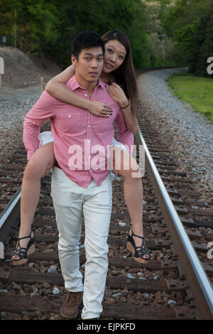 Romantisches asiatische paar spielen im Freien auf Eisenbahnschienen, reitet sie auf dem Rücken in einem "Huckepack" Mode Stockfoto