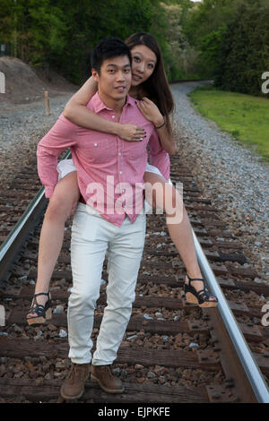 Romantisches asiatische paar spielen im Freien auf Eisenbahnschienen, reitet sie auf dem Rücken in einem "Huckepack" Mode Stockfoto
